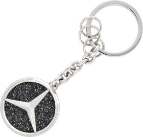 Schlüsselanhänger aus Metall mit dem Mercedes-Benz-Logo, auf einer glitzernden, schwarzen Oberfläche. 1