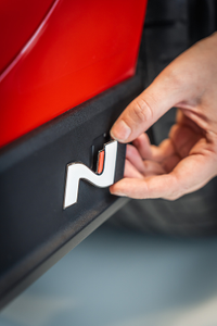 Hand eines Mechanikers, der ein N-Logo an der Seitenverkleidung eines roten Autos anbringt 1