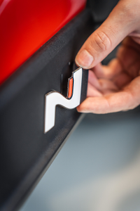 Hand eines Mechanikers, der ein N-Logo an der Seitenverkleidung eines roten Autos anbringt 3