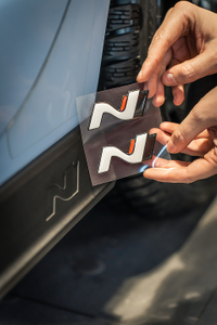 Mechaniker positioniert ein N-Logo mit transparenter Folie an der Seitenverkleidung eines Autos 2