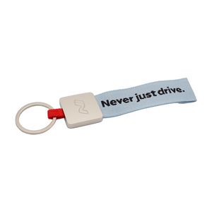 Schlüsselanhänger mit silbernem Metallclip und hellblauem Stoffband mit der Aufschrift ‚Never just drive.‘ sowie roter Stoffverbindung 1
