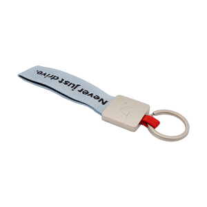 Seitenansicht des Schlüsselanhängers mit hellblauem Stoffband und Metallclip, graviertem N-Logo und Aufschrift ‚Never just drive.‘ 2