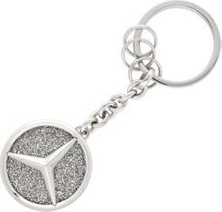 Schlüsselanhänger aus Metall mit dem Mercedes-Benz-Logo, auf einer glitzernden, silbernen Oberfläche